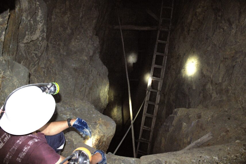 A miner observing a ladder installed in the middle of a cleft inside the hill.