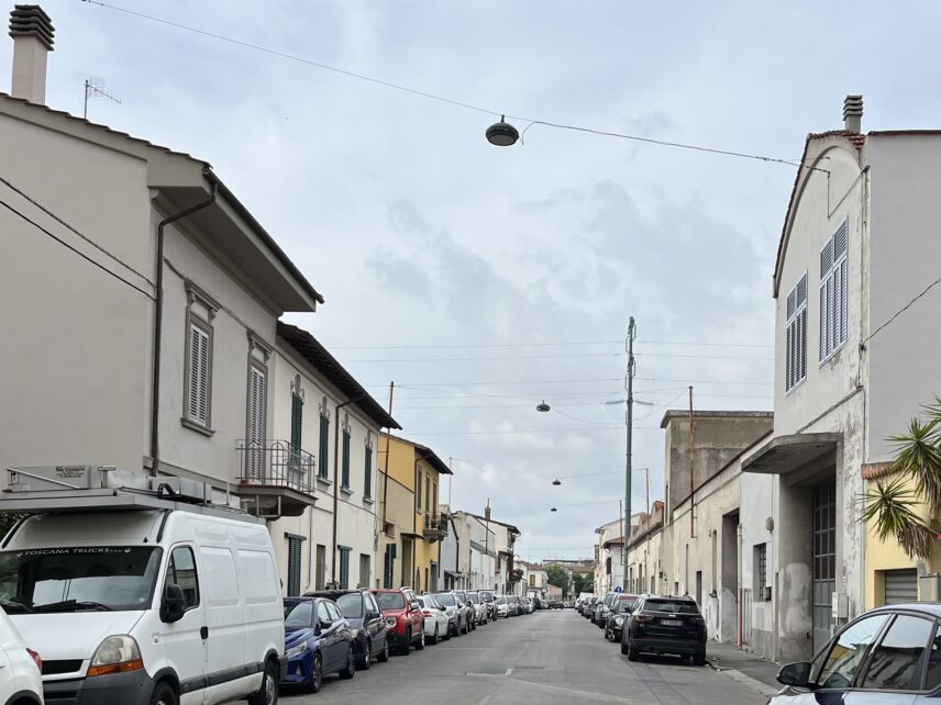 Narrow residential-industrial street in Prato with two-story buildings and parked cars.