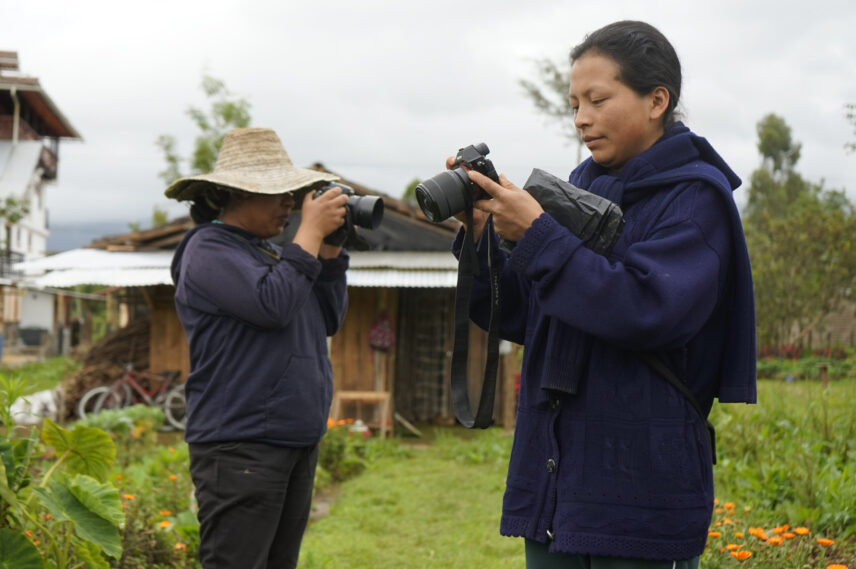 Two Kamëntšá women use cameras for creative documentation in the Tsebionán gardens.