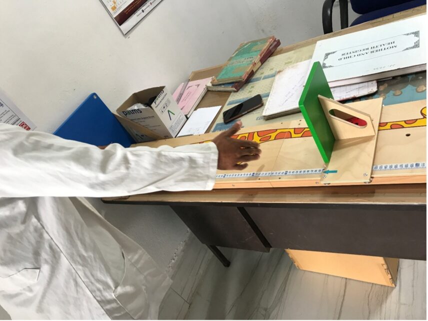 A photo of a person in a lab coat gesturing to a measuring device on a table