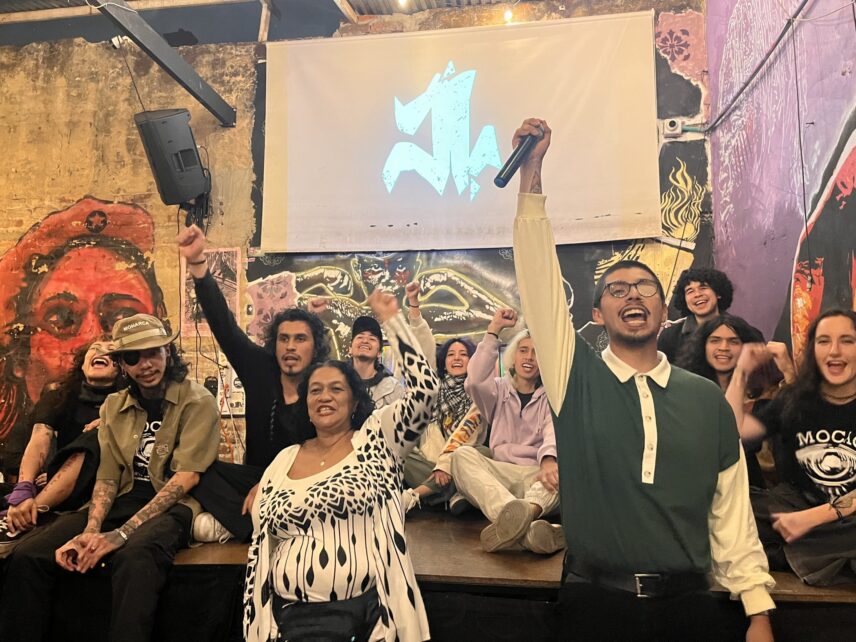 A group of eleven people gathered around a stage raising their fists in front of a screen and mural-covered walls