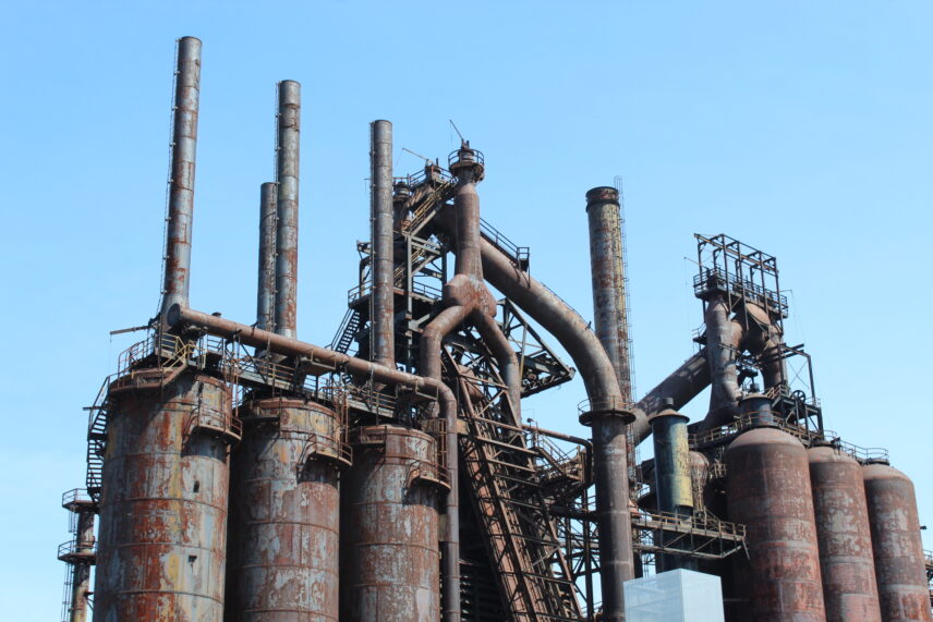 A towering, rusted, abandoned industrial structure in front of a blue sky
