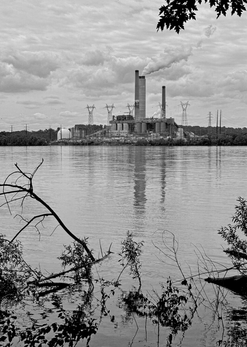 A slow-moving river with trees and a hydroelectric power station in the distance