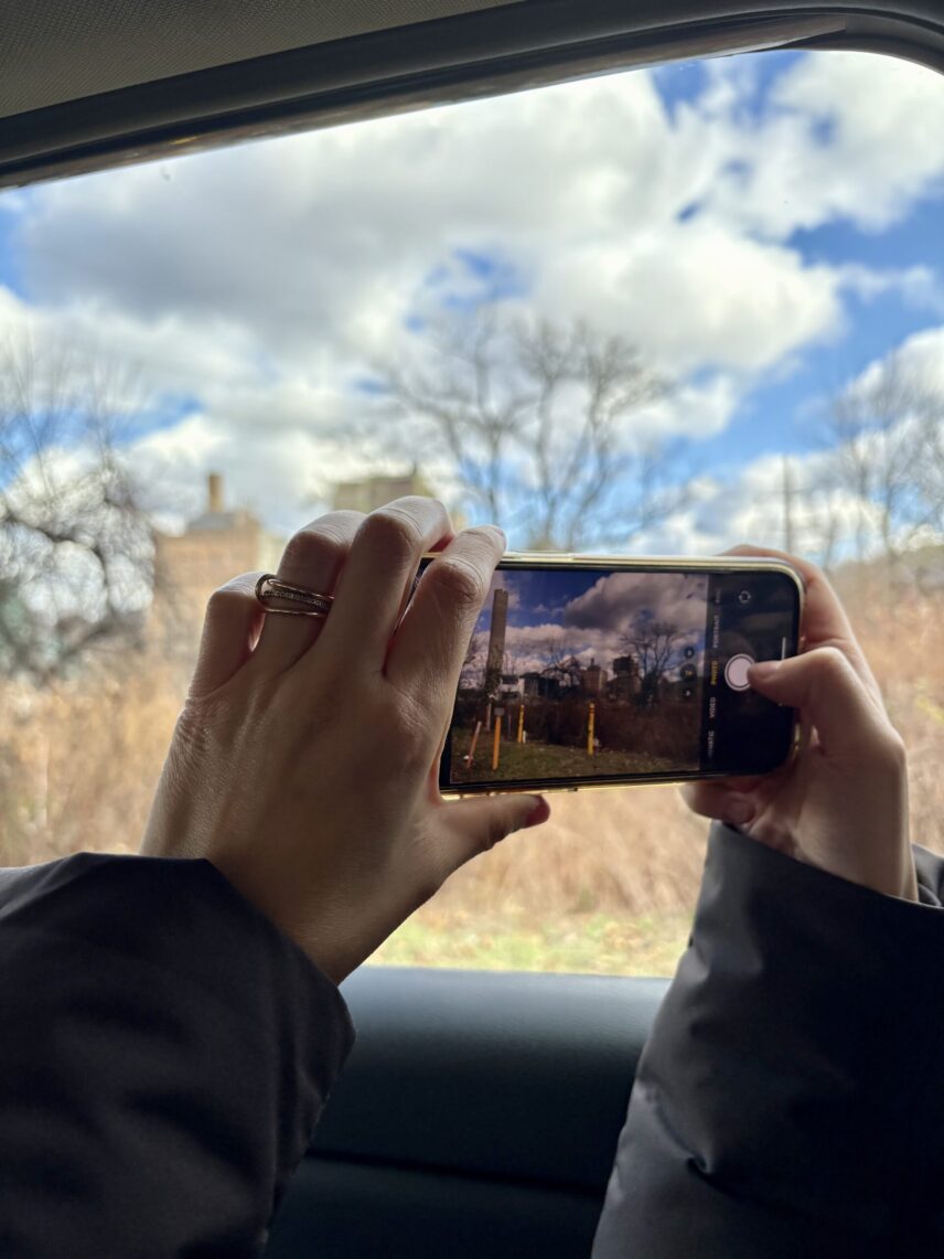 A pair of hands holds a smart phone taking a picture of a view through the window of a car