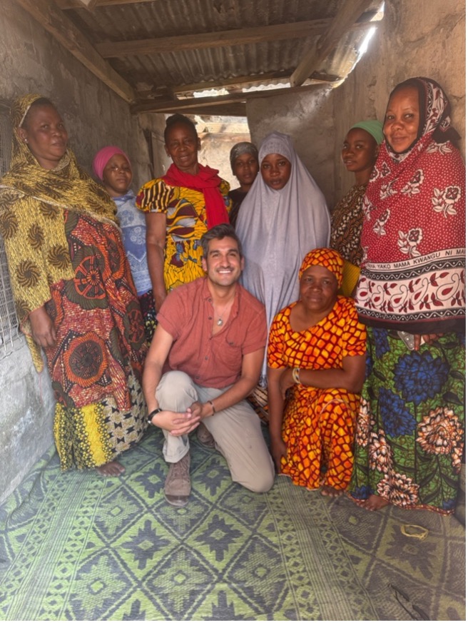 Alé Barrientos poses with a group of women wearing colorful patterned clothing and head coverings after a focus group in a home in Buguruni Ward, Dar es Salaam.