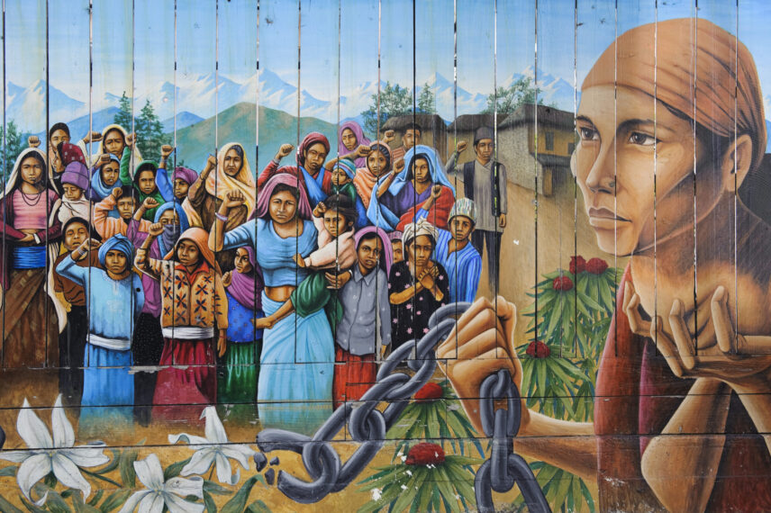 An image of a mural painted on fence boards that depicts a group of women and children with their right fists raised in the background, with a man in the foreground holding a broken chain.